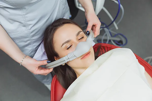 Dental assistant fitting a sedation mask over the nose of her calm female patient at Michael Regan, DMD Family, Cosmetic & Implant Dentistry in Milwaukie, OR